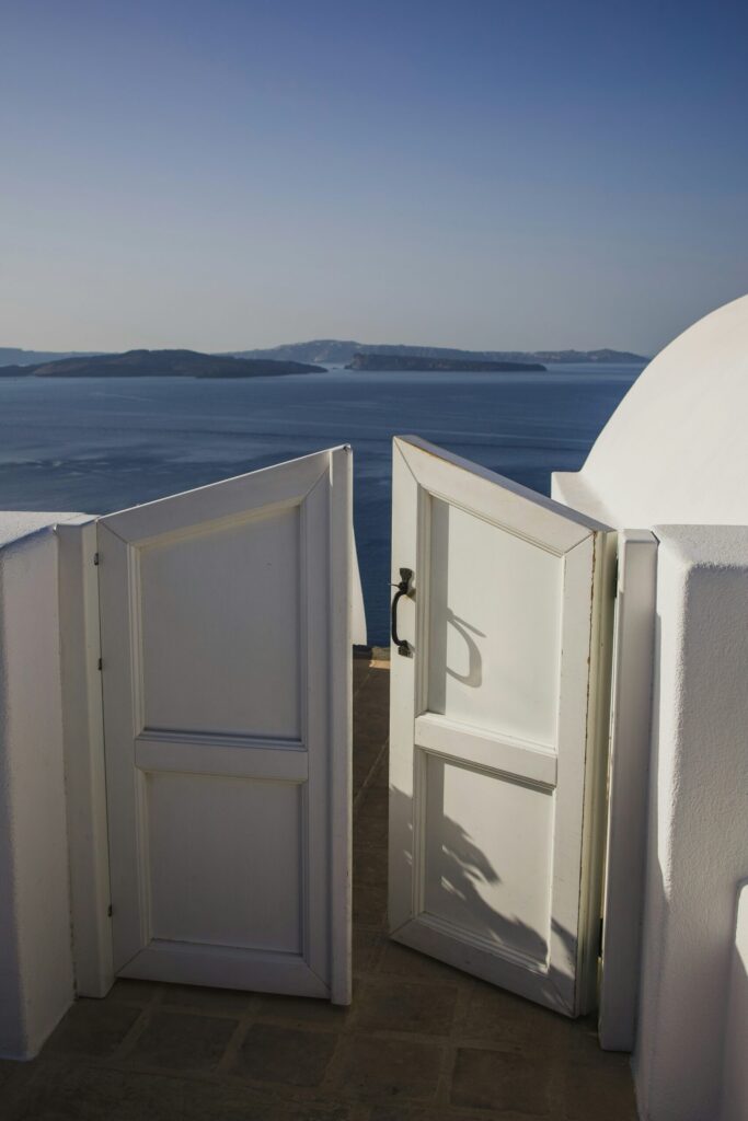白いドアが開いて青い海と空が広がるサントリーニ島の景色