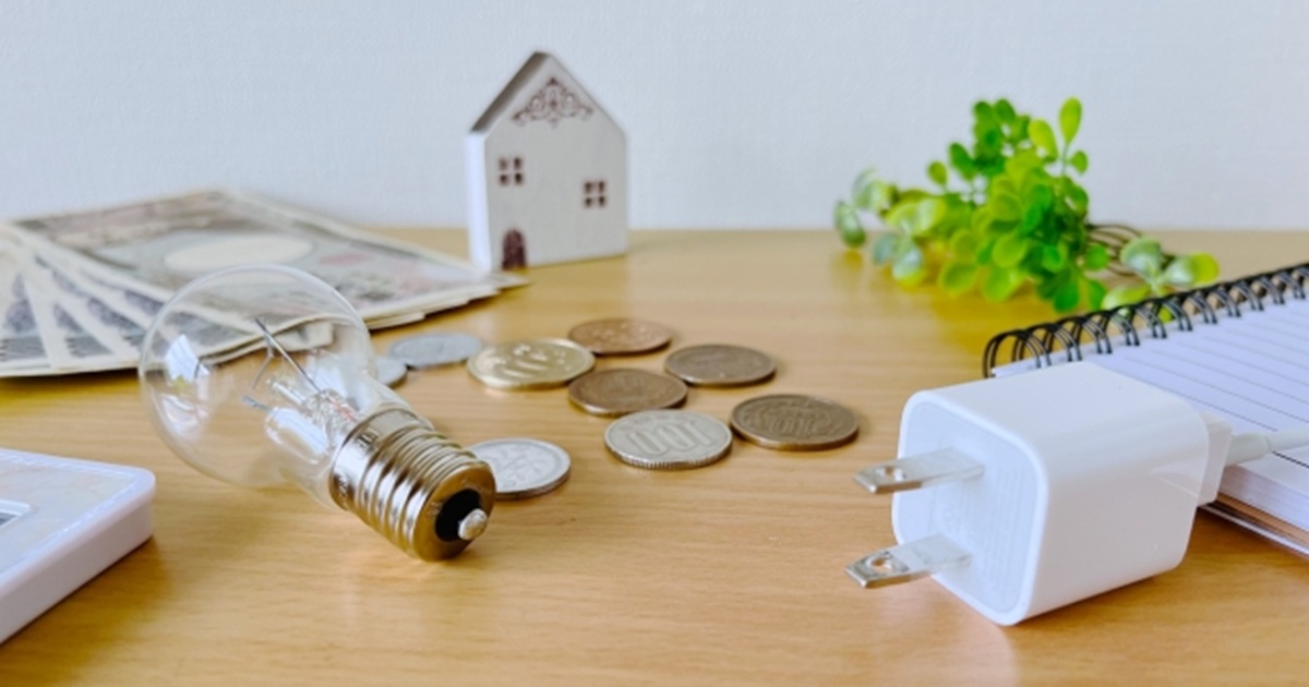電球・コイン・電源プラグ・お札が木製テーブルに並んだ電気代のイメージ